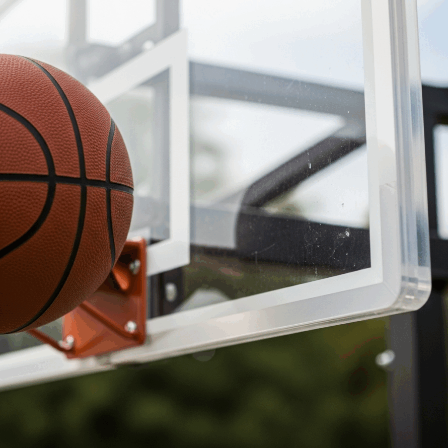 Close-up van een basketbal tegen een transparant polycarbonaat backboard, bevestigd met een metalen steun.