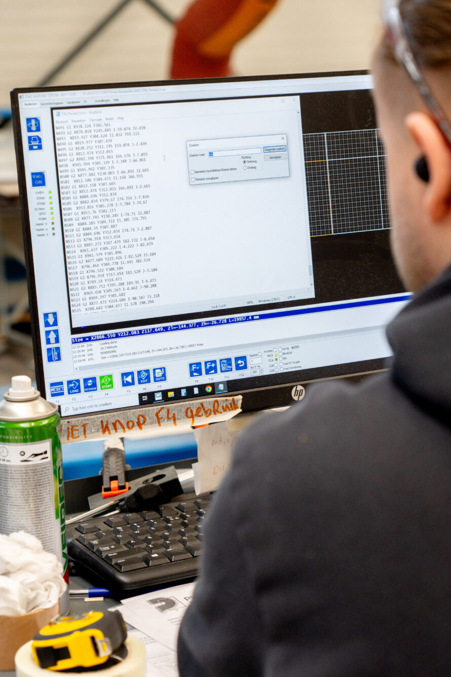 Medewerker werkt met CNC-software en productietekeningen op een computerscherm in de werkplaats.