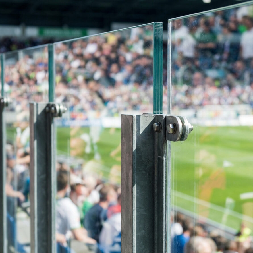 Polycarbonaat afscheidingspanelen met stalen montage in een vol stadion, geplaatst tussen tribune en speelveld.