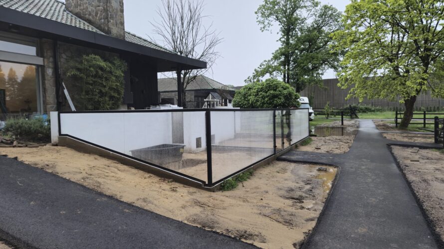 Glazen hoekafscheiding met zwarte frames rond een voortuin naast een moderne woning.