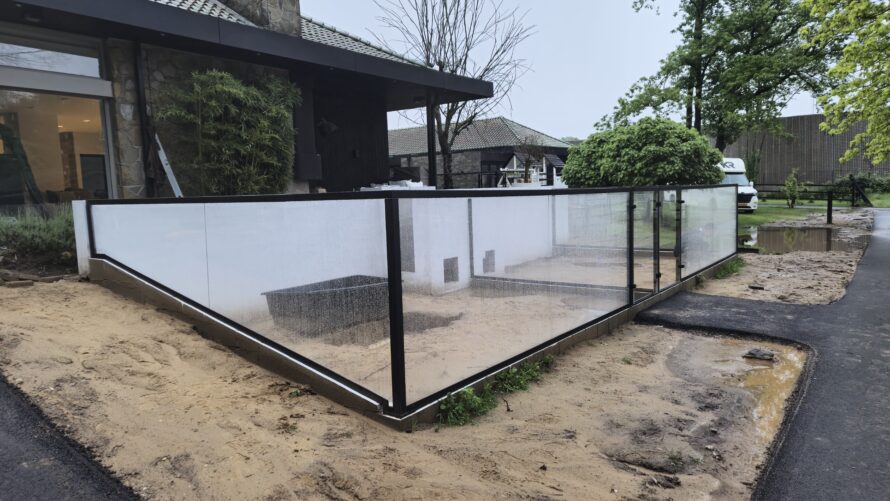Glazen hoekafscheiding met zwarte frames rond een voortuin bij een moderne woning, met blauwe selectierand en vinkje.