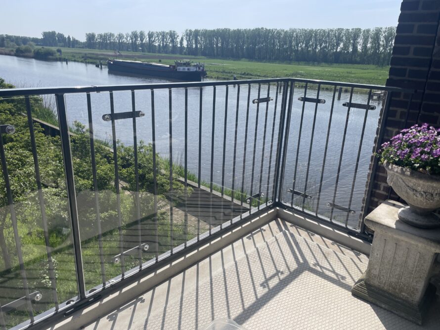 Uitzicht vanaf een balkon met metalen railing over een waterplas en een groen landschap.