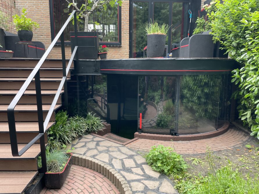 Tuin met trap en een moderne gebogen serre van plexiglas aan de woning.