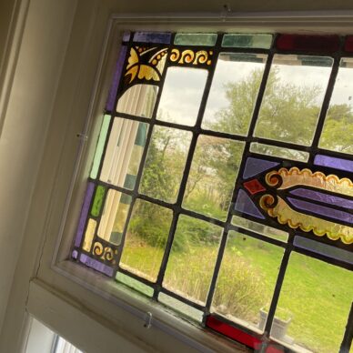 Glas-in-loodraam met decoratieve rand en uitzicht op groen buiten.