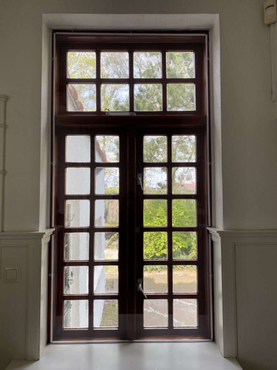 Donkere houten deur met glas-in-loodramen en zijpanelen.